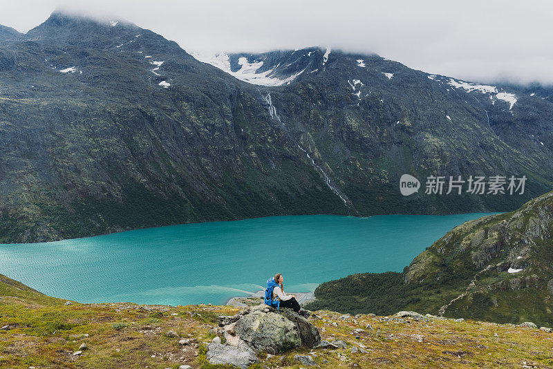 在挪威约顿海门国家公园，一名女子背着背包坐在山顶上凝视着群山