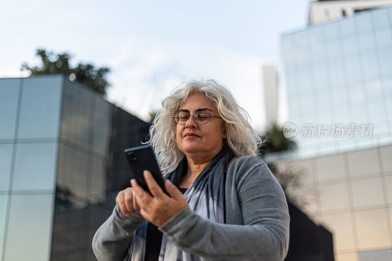 戴眼镜的女人在街上使用智能手机