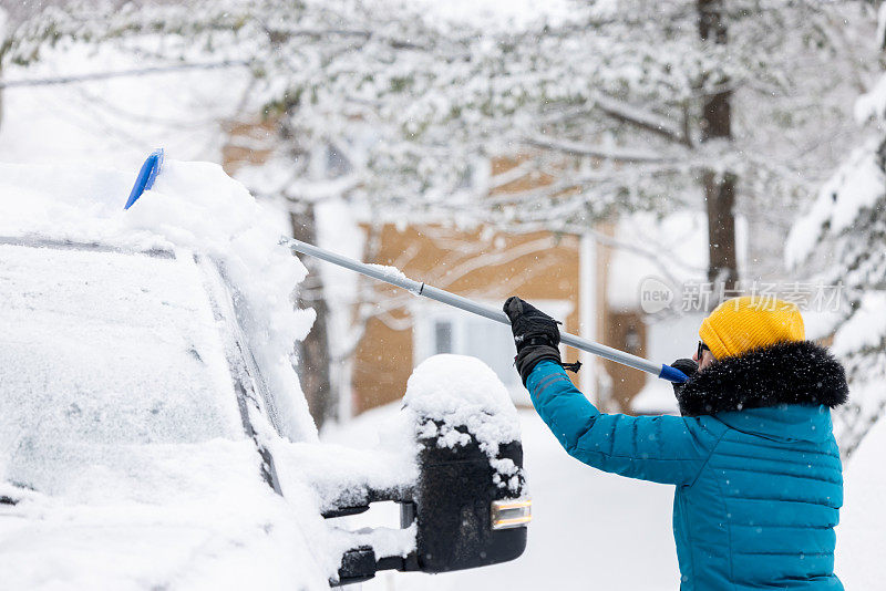 一名年轻女子在暴风雪后清理车上的积雪