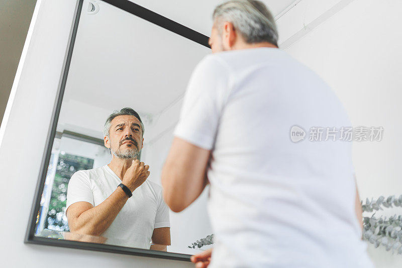 成熟的成年男子摸着胡子，看着镜子