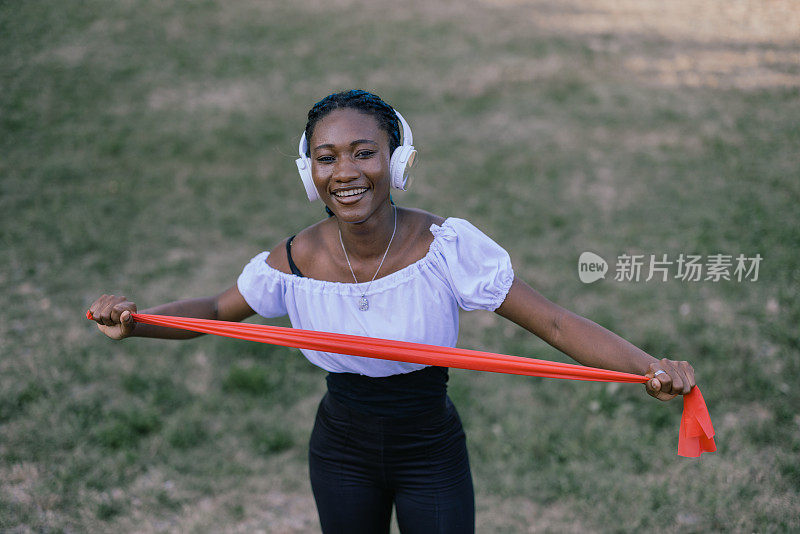 一位年轻英俊的非洲女运动员在公园里和一个抵抗乐队一起工作。