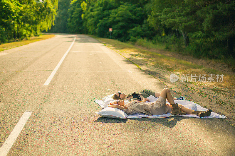 公路旅行。两个年轻的金发女孩在森林里的旧公路上玩得很开心。