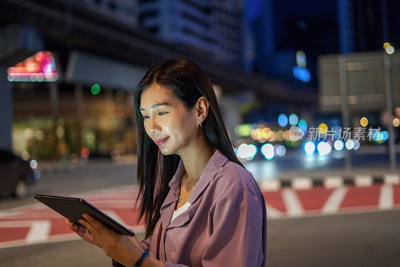 晚上在城市街道上使用电子平板电脑的女商人