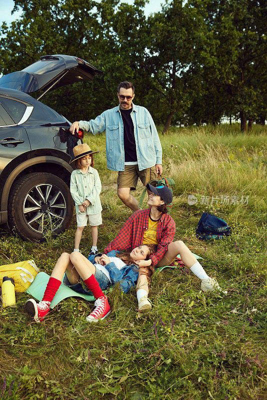 美丽的家庭，男人，女人和孩子坐在汽车健身matt和休息后积极爬山。户外，自然休息