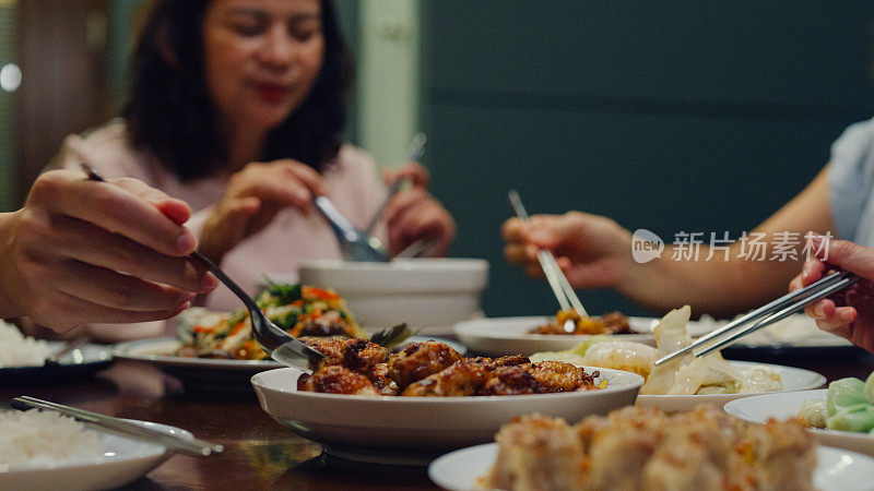 亚洲家庭吃中国菜的特写，晚上坐在家外后院的餐桌旁吃晚饭。多代同堂的家庭一起享受消费。