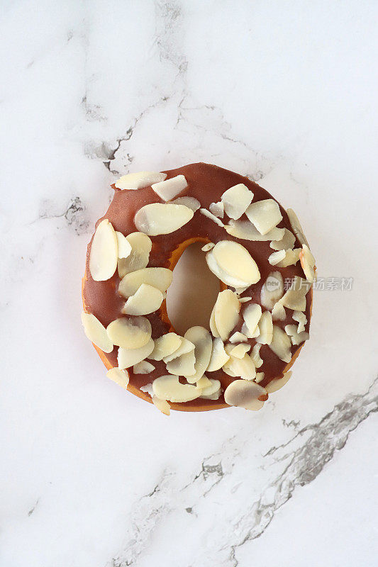 个人形象，巧克力釉面环甜甜圈，用杏仁仁片装饰的油炸甜点，大理石效果背景，高架视图