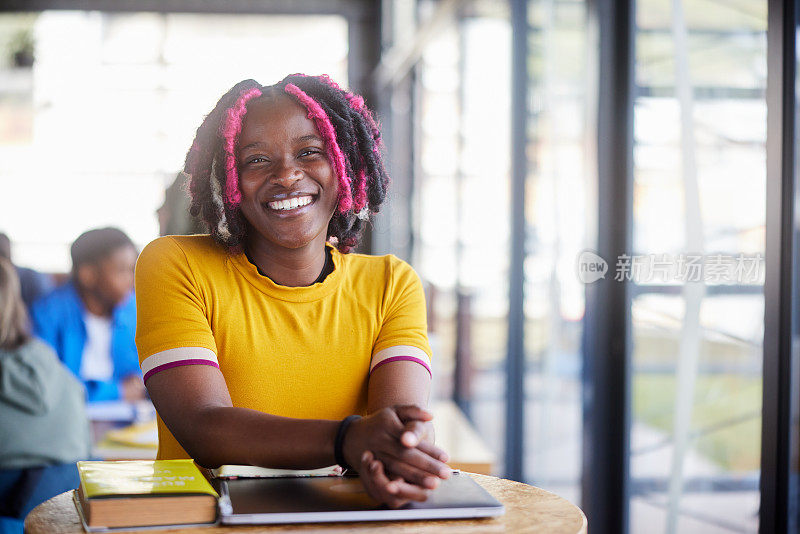 一个微笑的女大学生坐在自助餐厅的桌子旁