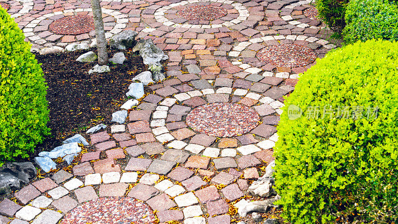 在房子附近和花园里铺设圆形小路。用于花园小径的铺路石的原始变体。红白相间的花岗岩走道呈圆形布局。创意铺装范例