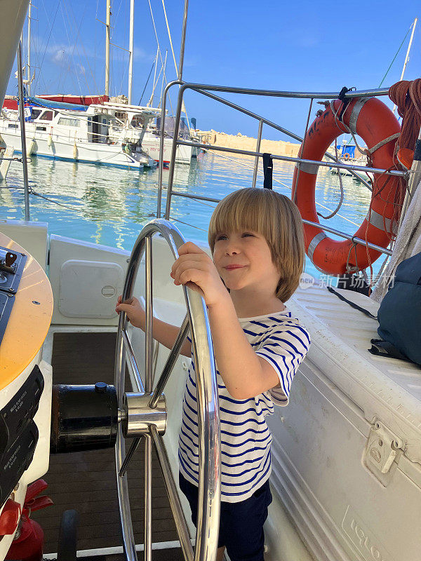 可爱的男孩掌舵一艘帆船。家庭的游艇。孩子们在小船长游艇上