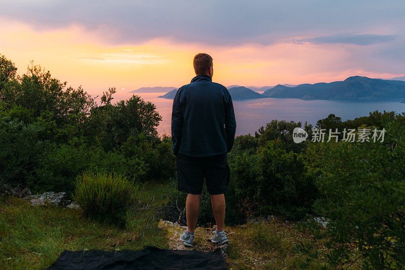 一名男子在土耳其欣赏神奇的日落，俯瞰大海和山脉