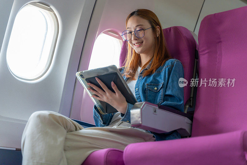 快乐的年轻女子在飞机上独自坐在窗边玩着她的平板电脑