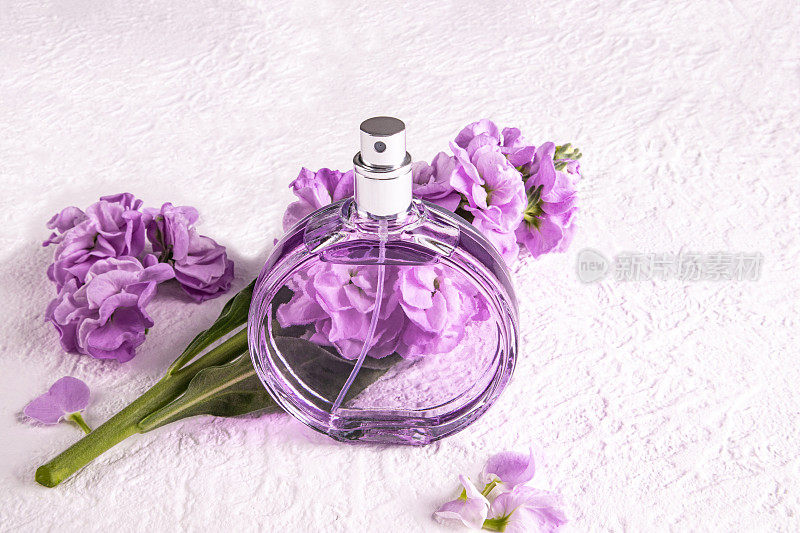 一瓶别致的女士香水和一朵精致的丁香色花。前视图。未命名的瓶子用于产品介绍。白色背景