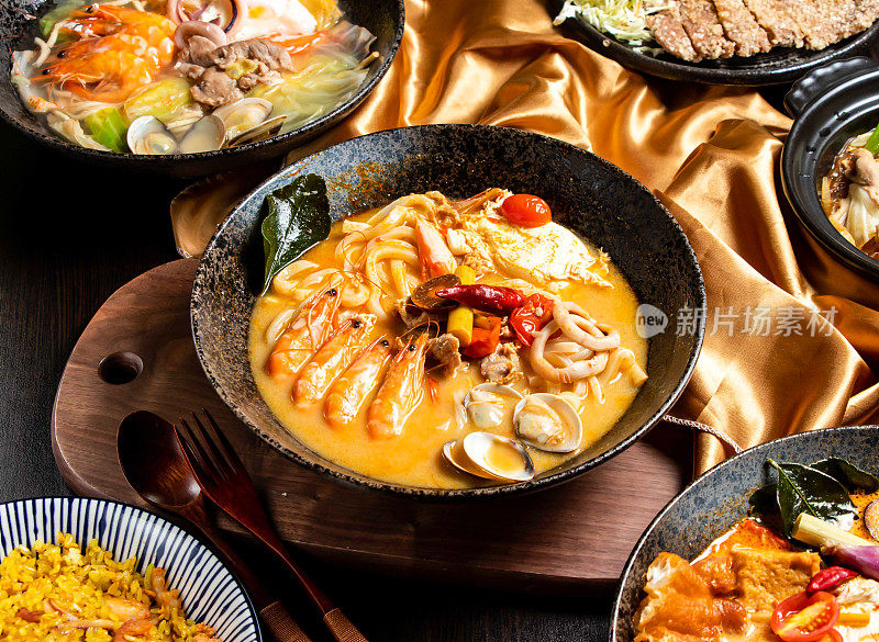 泰式酸辣海鲜和鸡肉用叉子和勺子炖在盘子里，放在木板上，亚洲食物的侧视图