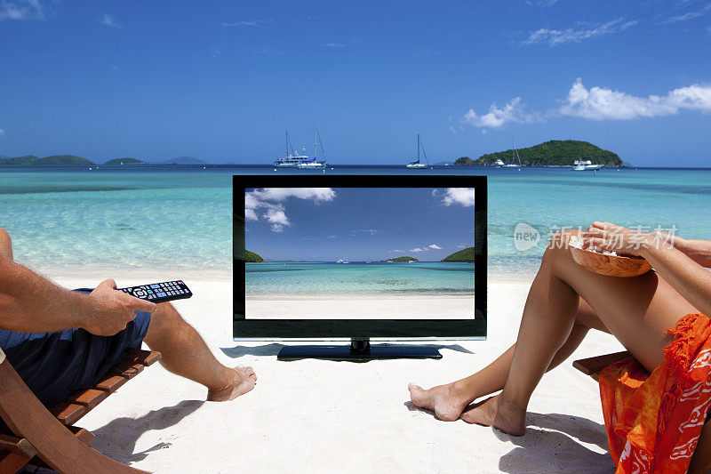 一对夫妇正在加勒比海的热带海滩上看电视