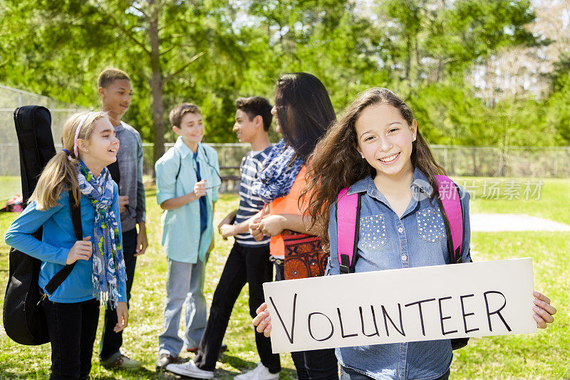 青少年:拉丁女孩举着“志愿者”的牌子。群的朋友。