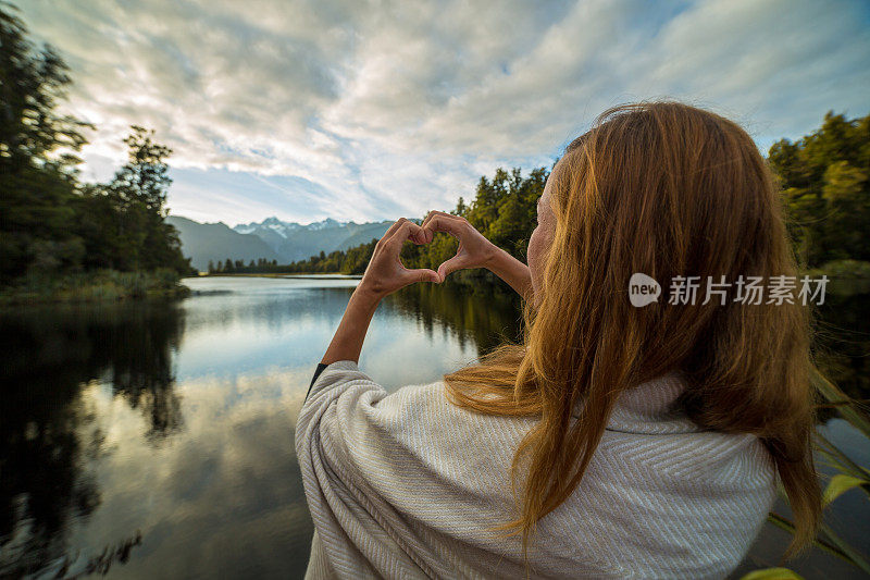 女人在山湖景观上做心形指架