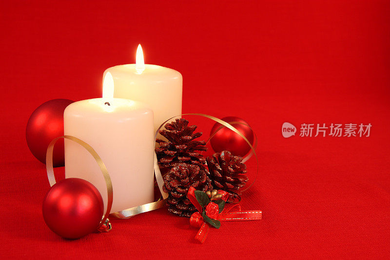红色的圣诞装饰物，点燃的蜡烛上横放着松果
