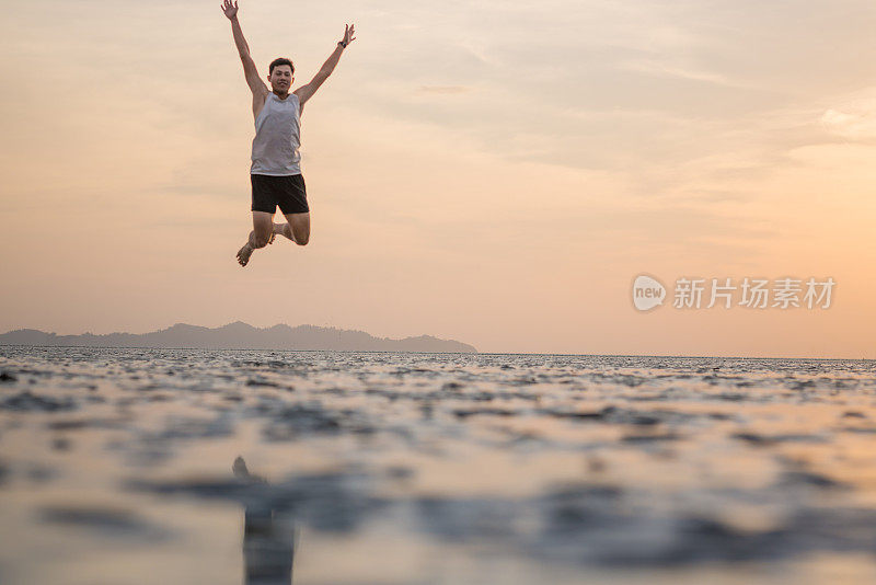 年轻的亚洲男子在海滩上奔跑，夕阳为背景