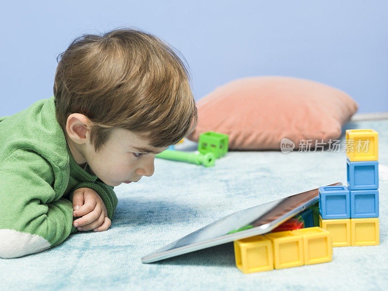 坐在地毯上使用平板电脑的小男孩