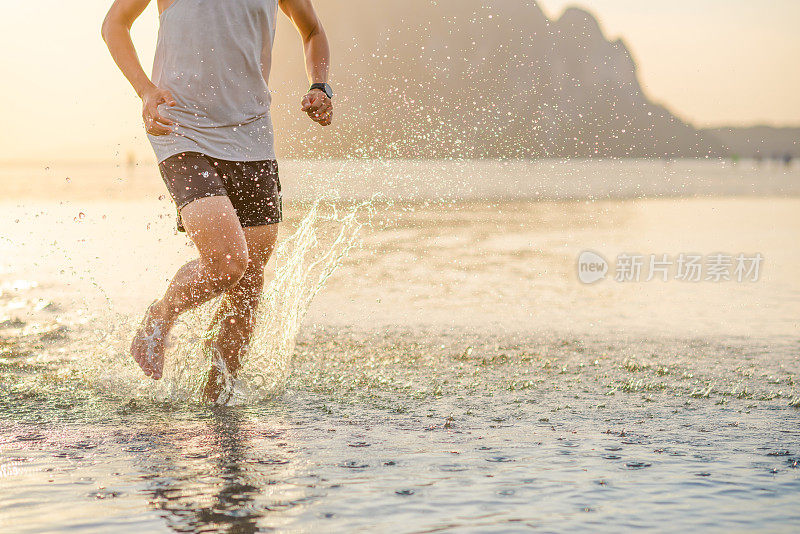 年轻的亚洲男子在海滩上奔跑，夕阳为背景