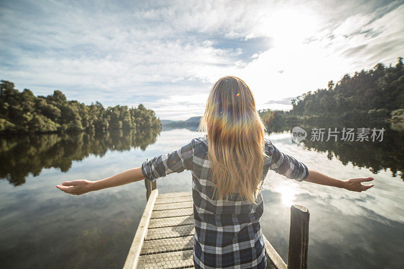 年轻女子在湖上的防波堤上放松，双臂伸展