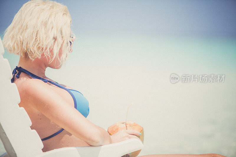 迷人的金发女人坐在和日光浴在浅水，马尔代夫