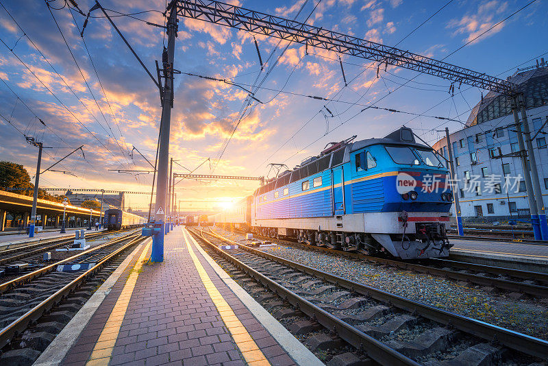 日落时分火车站的蓝色火车。令人惊叹的工业景观，老机车，老建筑，铁路和彩色的日落天空与云。火车在铁路上。美丽的铁路平台