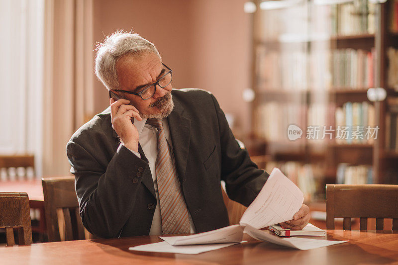 一个成熟的商人在办公室一边看报告一边打电话。