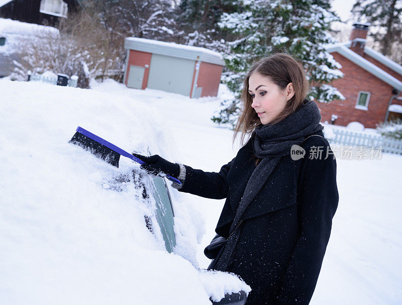 冬天即将来临。女人在冰冷的天气里，车被雪覆盖着。