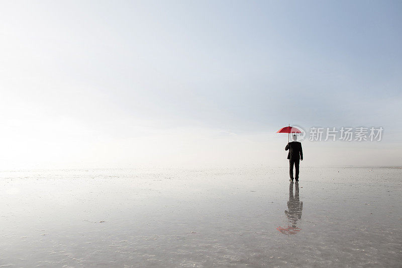 在盐湖上，穿着黑色西装，打着红色雨伞的商人