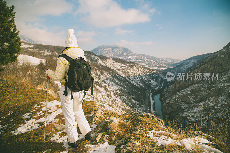 近景美丽的年轻女子在冬天的衣服站在一边，手拿木棍的背景雪山