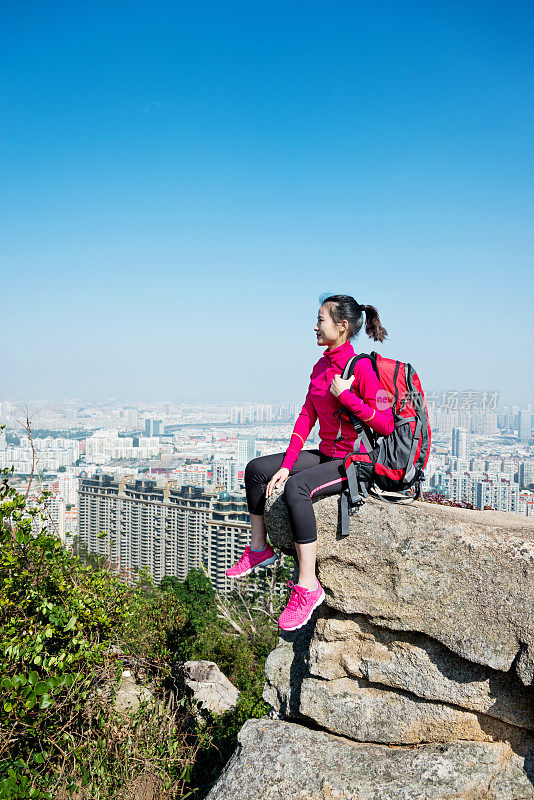 女背包客坐在山顶的岩石上