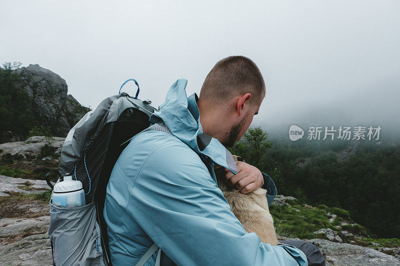 背着背包的男子和狗在挪威的布道石徒步旅行后休息