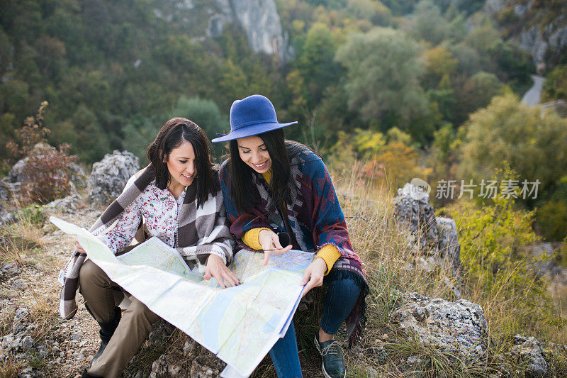 两个女孩看着以山为背景的地图，思考着该往哪里走