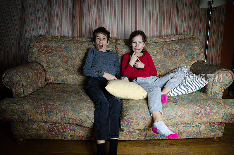 两个孩子坐在客厅的沙发上看电视时被吓到了