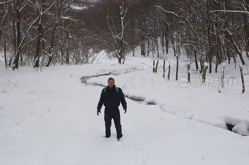 快乐的成年人徒步旅行在下雪的冬天大自然旁边流动的小溪在森林里