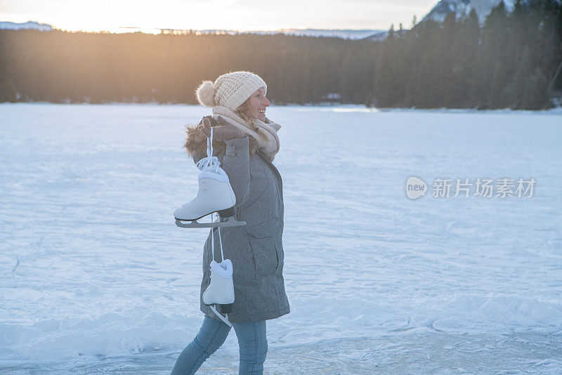 夕阳西下，年轻女子肩挎冰鞋走在结冰的湖面上，享受着寒假的乐趣