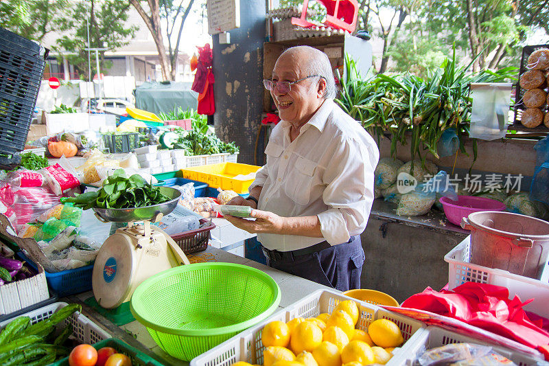 一位年长的亚洲蔬菜摊主在为他的顾客计算价格