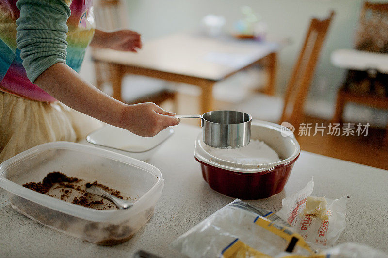 小女孩在厨房柜台上用金属量杯烘焙