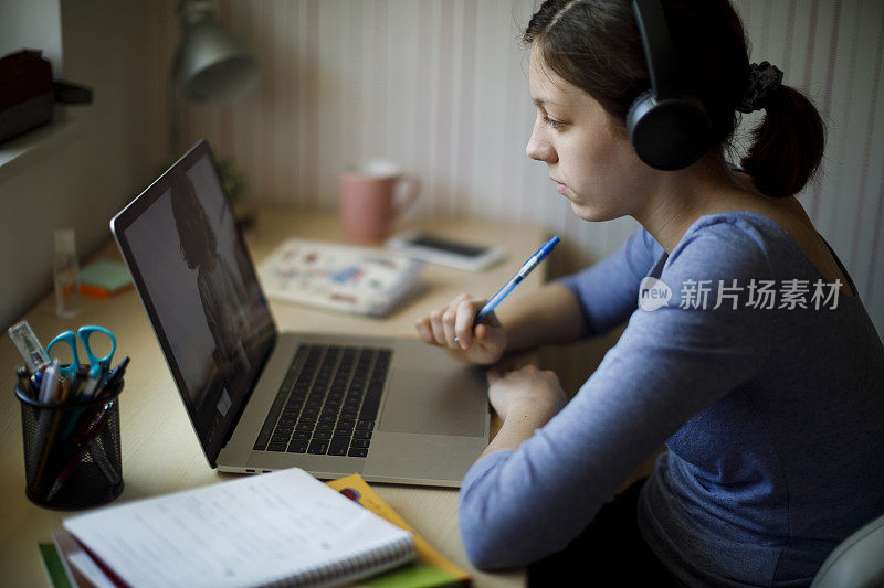 十几岁的女孩戴着耳机和笔记本电脑在家里在线上课