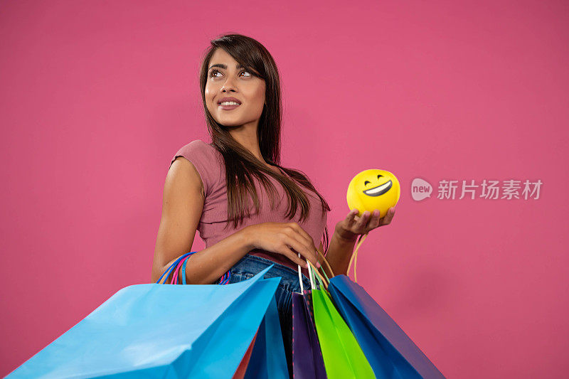 美丽的年轻女子购物袋和笑脸，笑的表情在她的手，粉红色的背景。购物概念，夏季大甩卖
