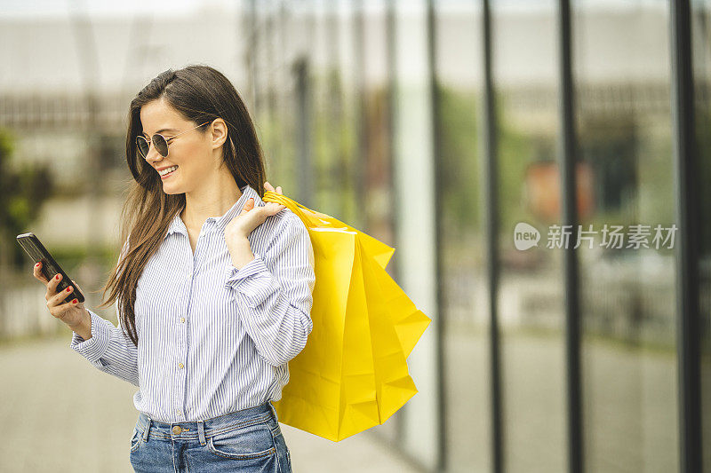 年轻漂亮的女人提着购物袋，用智能手机走路