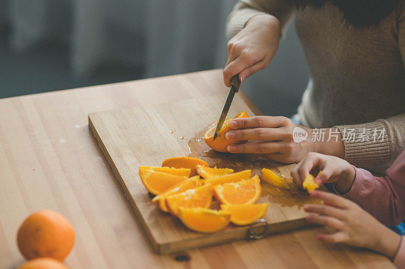年轻的亚洲母亲和她的女儿在客厅里享受橘子