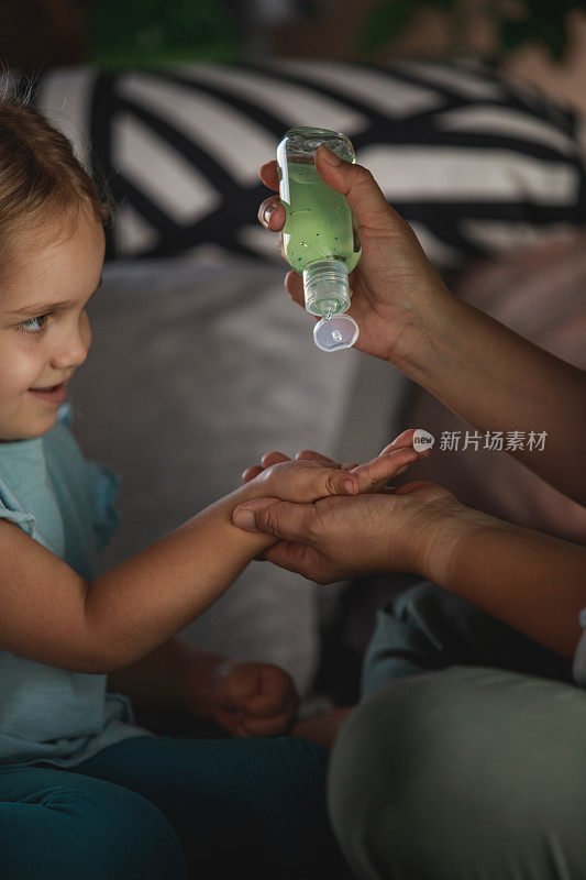 一名妇女教她蹒跚学步的孩子在流感大流行期间洗手液的重要性