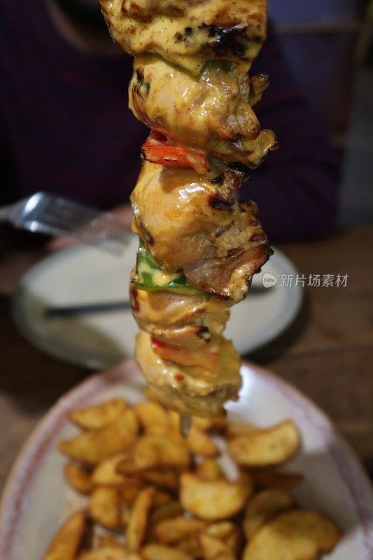 这是烤鸡肉串的特写，烤鸡胸肉串在红绿辣椒上，淋上辣酱