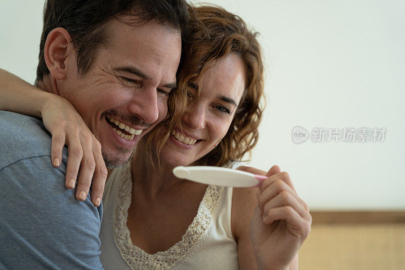 一对微笑的夫妇在卧室里看验孕试纸