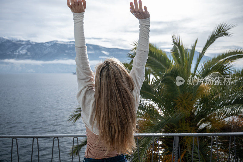 年轻女子伸展她的身体在阳台上的早晨，湖的景色