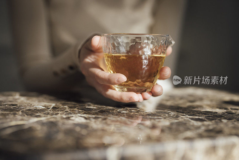 泡茶:一个女人的手拿着一个装满绿茶的杯子