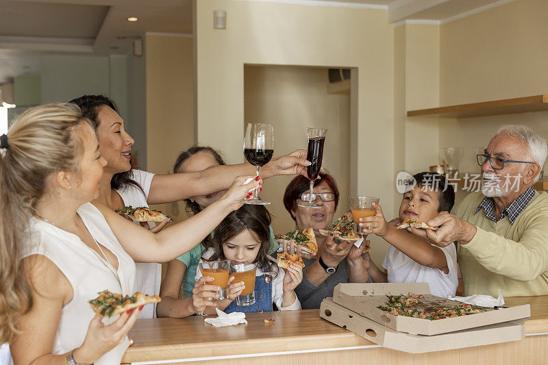 三代同堂吃披萨，举杯共饮，享受时光。幸福家庭的概念，在一起，和乐趣。