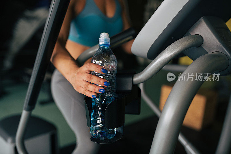 年轻女子拿着水瓶和锻炼在aa健身房。